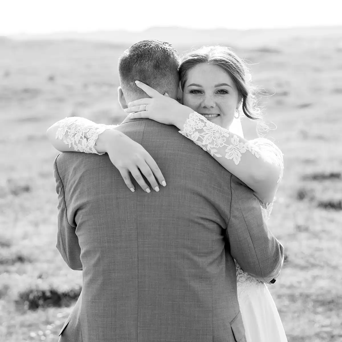 Intieme zwart-wit trouwfoto van een bruidspaar dat elkaar omhelst tijdens een fotoshoot in de duinen van Den Helder