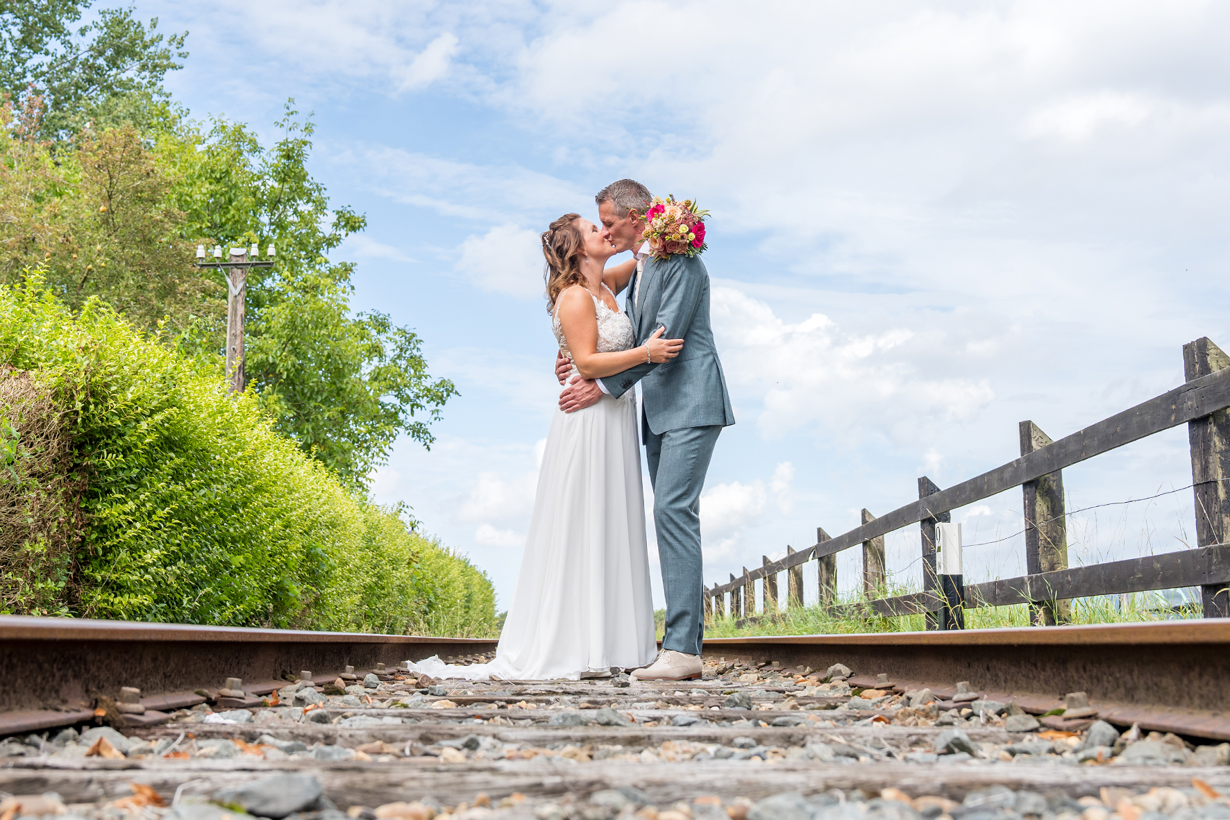 Zolang een romantische kus tussen bruid Mirjam en bruidegom Wouter op het spoor van het historische station in Twisk, vastgelegd door Daniel Vos Fotografie.