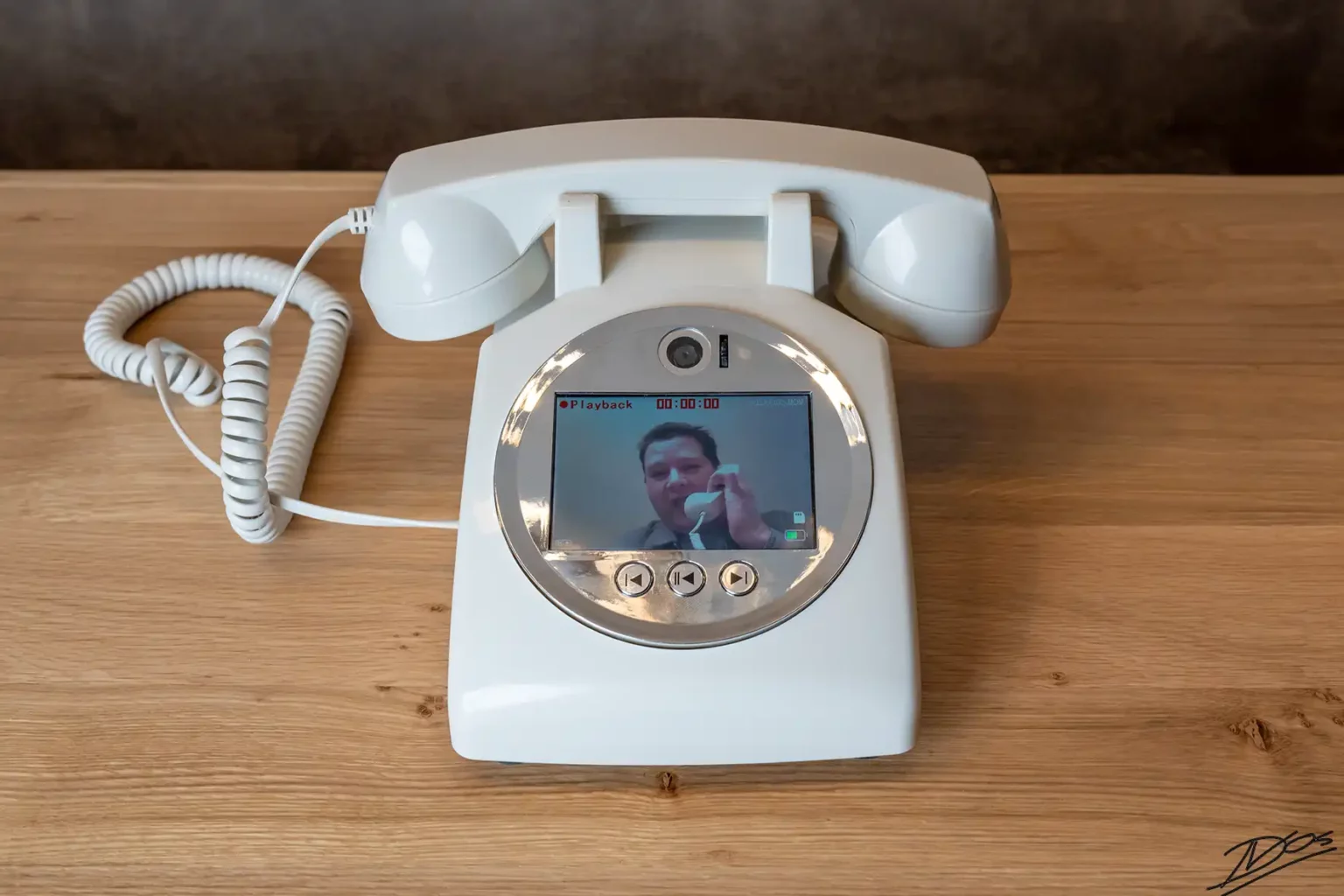 Vooraanzicht van een witte retro telefoon als videogastenboek met een actief schermpje waarop een ingesproken videoboodschap wordt afgespeeld.